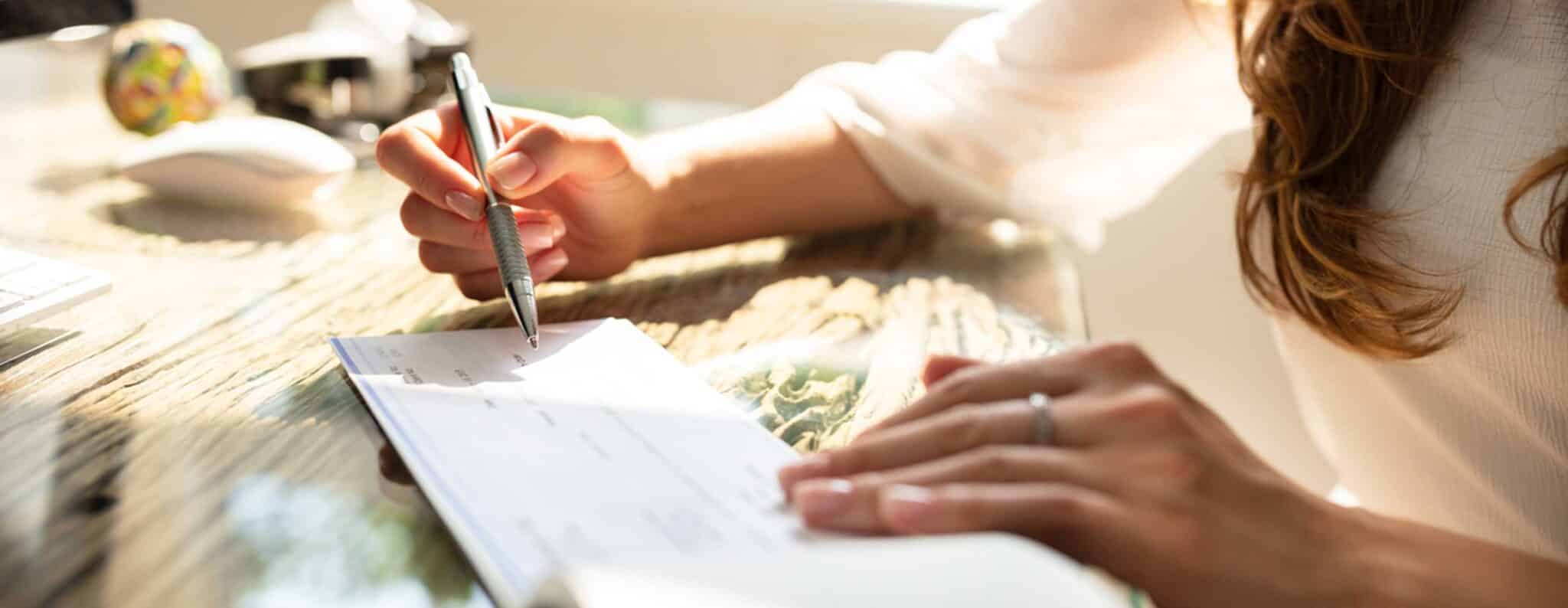 A hand writing a check at a desk
