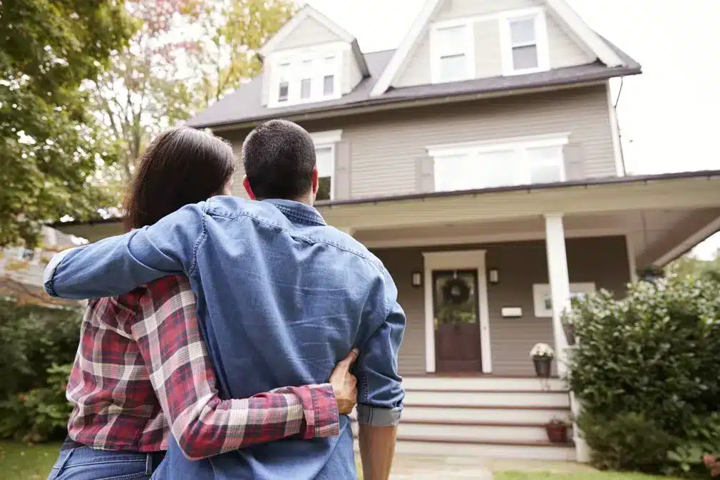 Man and woman with arms around each other standing in front of a house